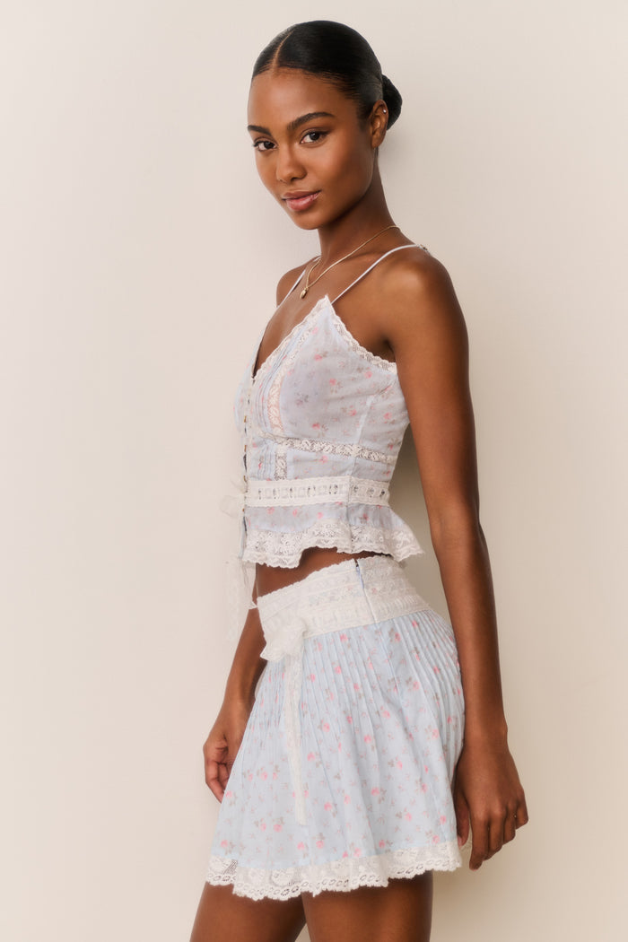 Woman wearing a Skirt and top with blue floral pattern and white lace trim with a beige background
