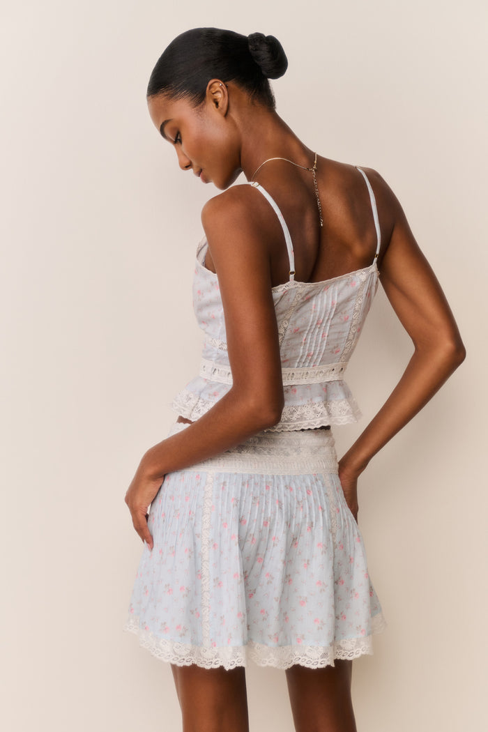 Woman wearing a Skirt and top with blue floral pattern and white lace trim with a beige background