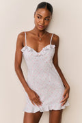 Woman wearing a blue floral ruffle hem mini dress with thin straps against a beige background
