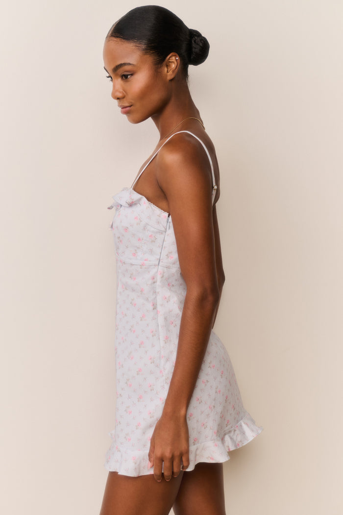 Woman wearing a blue floral ruffle hem mini dress with thin straps against a beige background