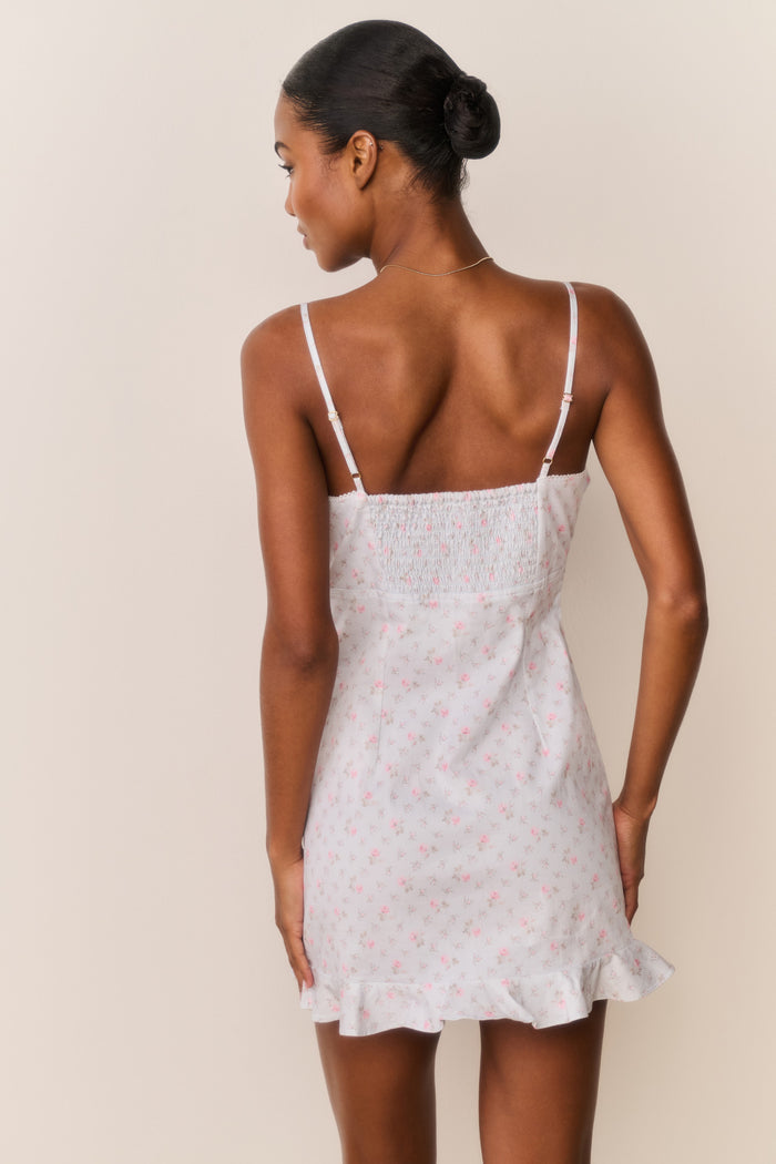 Woman wearing a blue floral ruffle hem mini dress with thin straps against a beige background