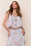 Woman wearing a light blue ruffled floral top and skirt set against a beige background