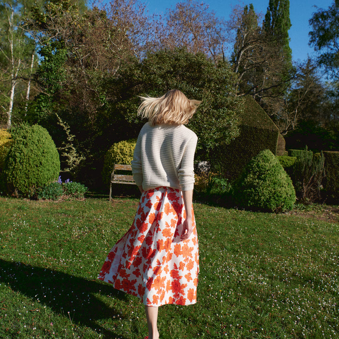Woman in a garden wearing a floral skirt and light sweater