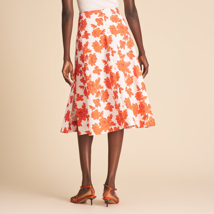 Woman wearing a white cardigan, floral skirt, and high-heeled shoes on a beige background