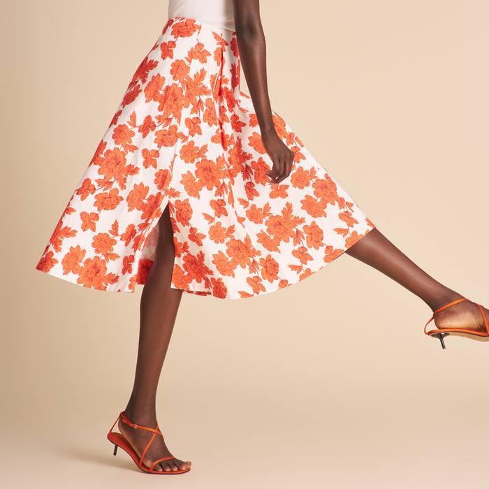 Woman wearing a white cardigan, floral skirt, and high-heeled shoes on a beige background
