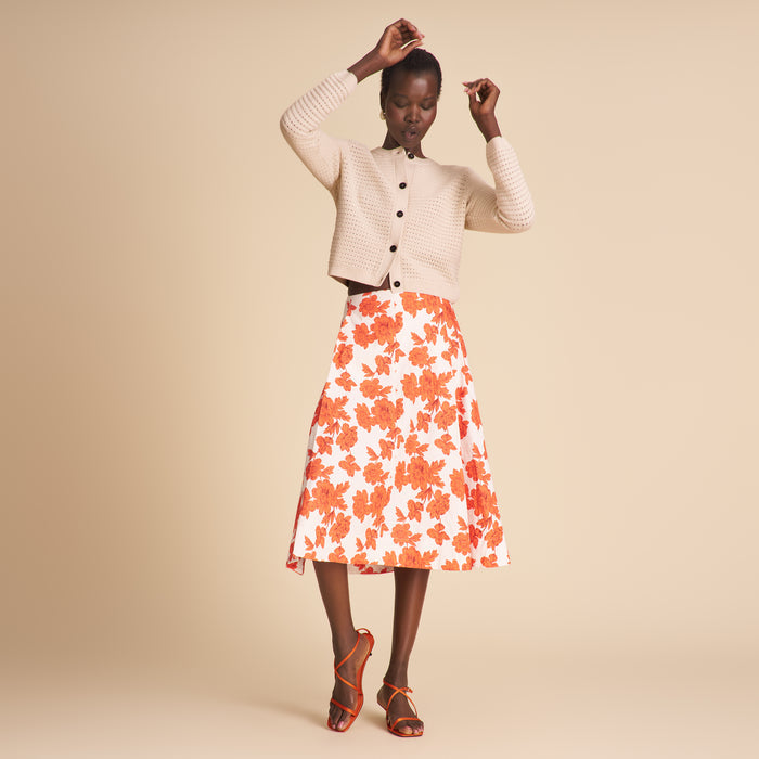 Woman wearing a white cardigan, floral skirt, and high-heeled shoes on a beige background