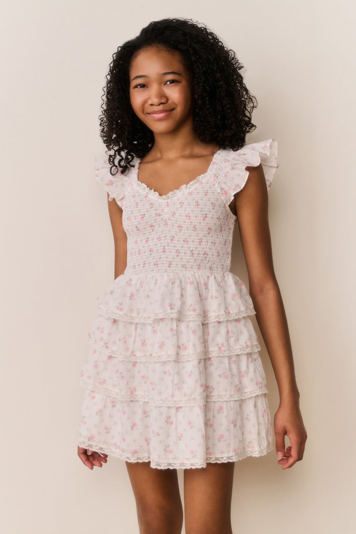 Girl wearing beige ruffle dress with pink floral pattern on a white background