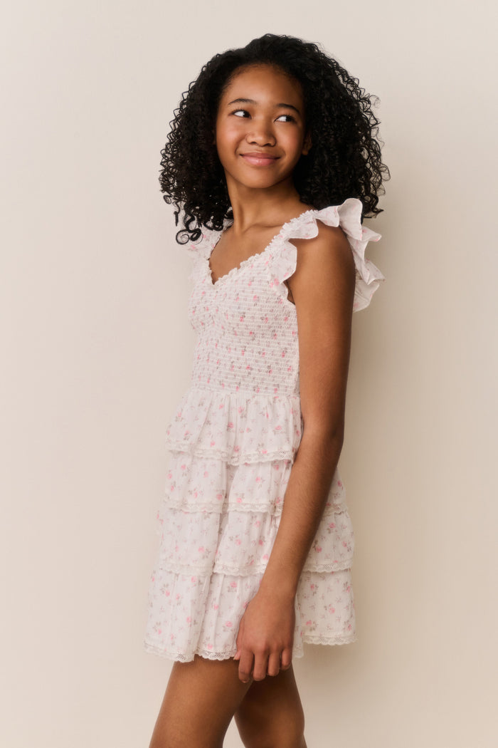Girl wearing beige ruffle dress with pink floral pattern on a white background
