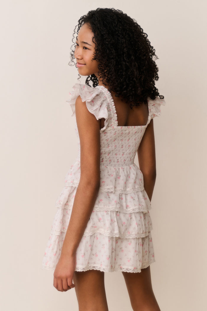 Girl wearing beige ruffle dress with pink floral pattern on a white background