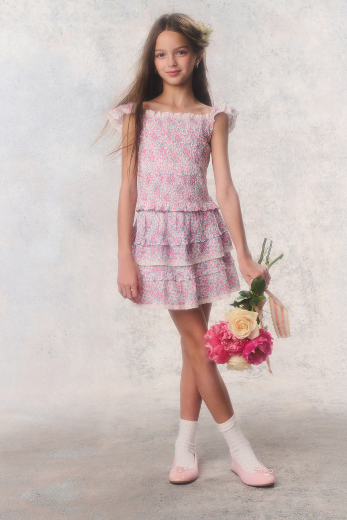 Young girl in a floral dress holding flowers against a plain background