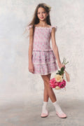 Young girl in a floral top and skirt holding flowers against a plain background
