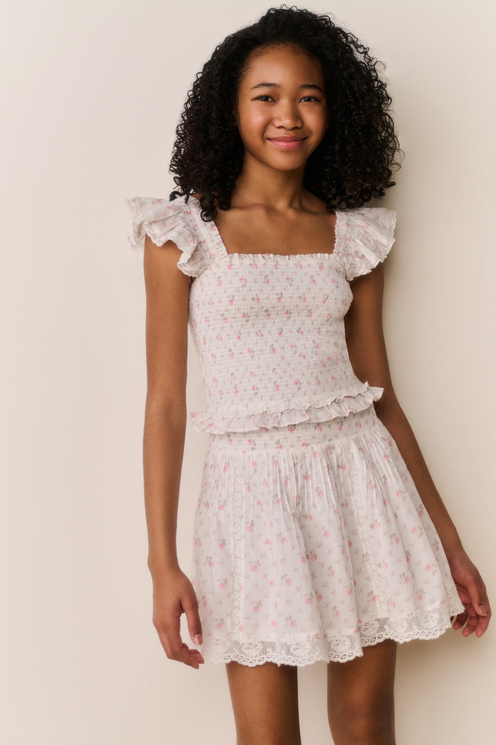 Girl wearing white floral ruffle shirt and matching skirt against white background