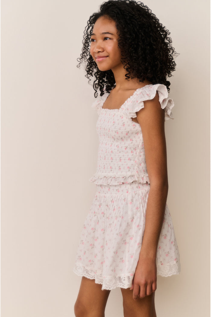 Girl wearing white floral ruffle shirt and matching skirt against white background
