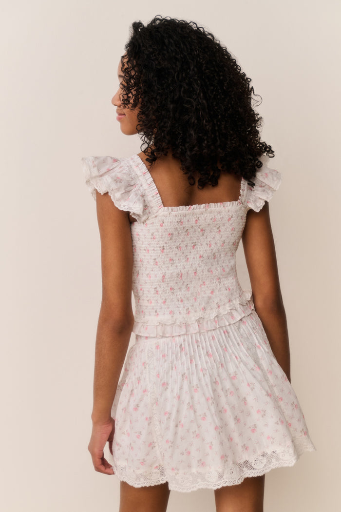 Girl wearing white floral ruffle shirt and matching skirt against white background