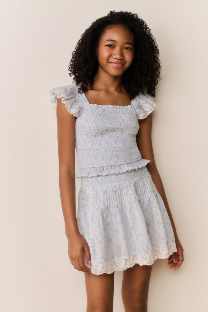 Young girl wearing Light blue floral pattered skirt with lace trim and matching shirt with ruffled details on a beige background