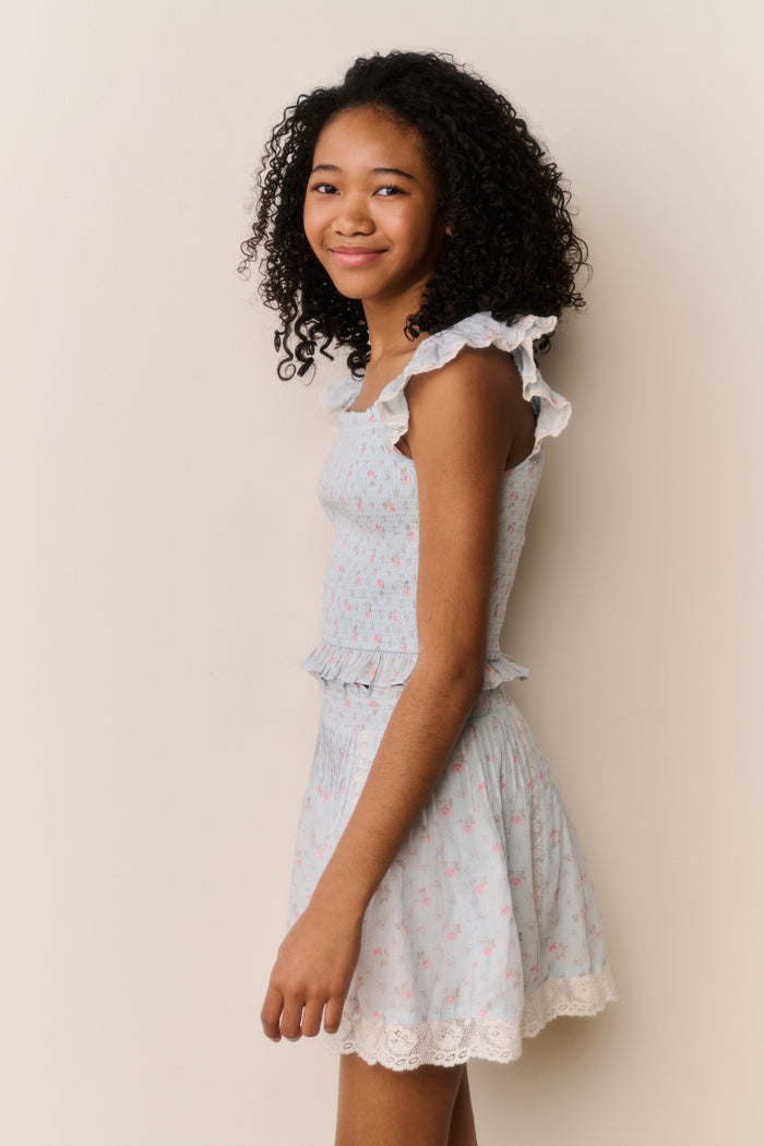 Young girl wearing Light blue floral pattered skirt with lace trim and matching shirt with ruffled details on a beige background