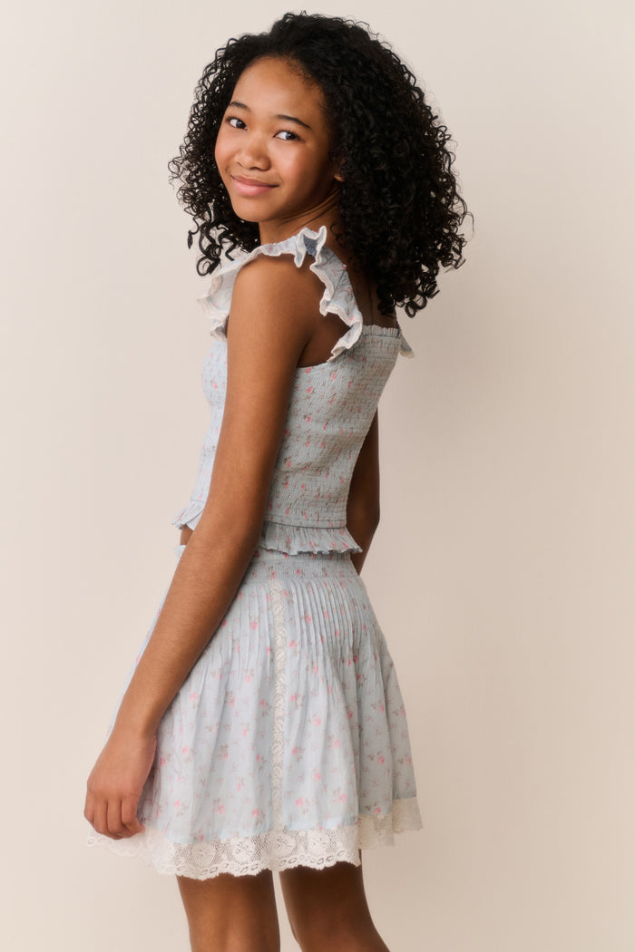 Young girl wearing Light blue floral pattered skirt with lace trim and matching shirt with ruffled details on a beige background