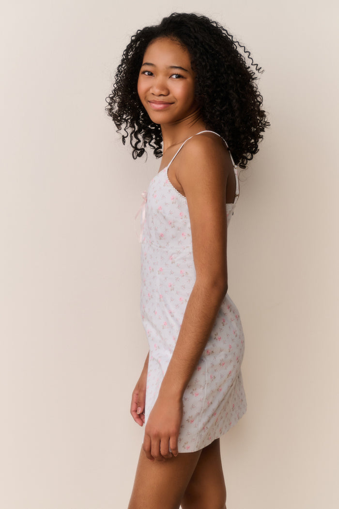 Tween wearing a blue floral dress against a beige background