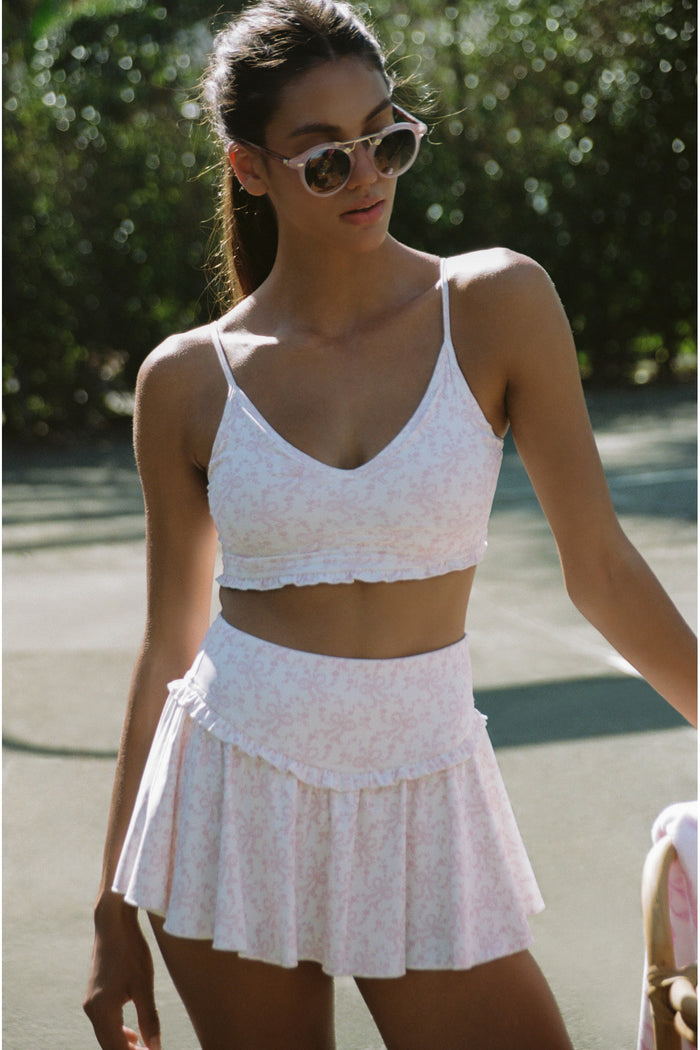 Woman wearing a white and pink two-piece outfit with sunglasses outdoors.