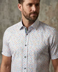 Man wearing a short-sleeve shirt with a colorful pattern against a textured wall.