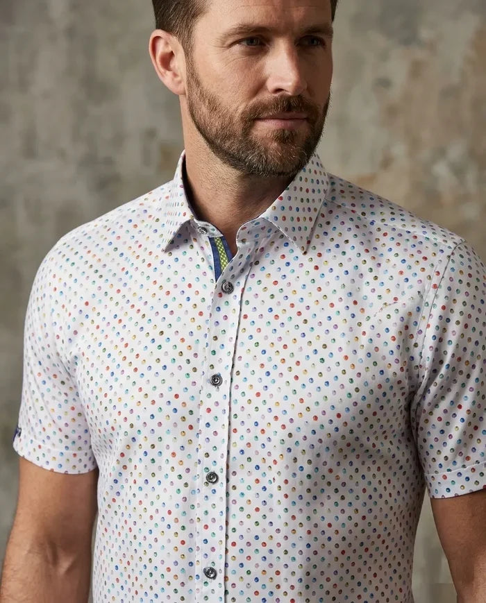 Man wearing a short-sleeve shirt with a colorful pattern against a textured wall.