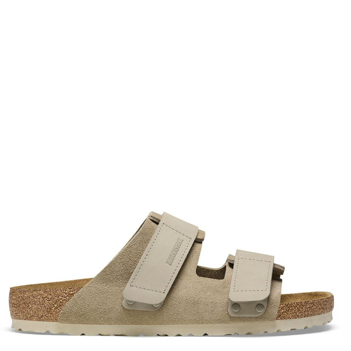 A pair of beige Birkenstock sandals with suede upper and nubuck hook-and-loop straps, featuring a cork-latex footbed.