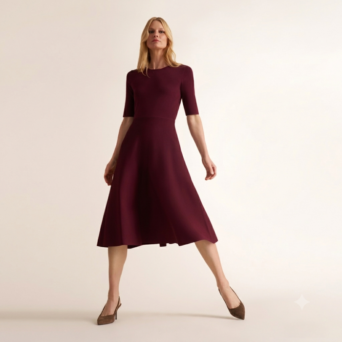 A woman modeling a short-sleeve, knee-length A-line dress in deep burgundy against a plain, warm off-white studio background. | Lead